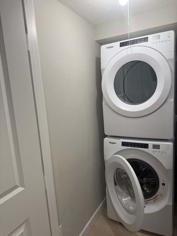 A stacked washer and dryer unit in a laundry room with white walls and a door on the left. - Radiant 2bedroom, 1bath Suite, in Calgary central area, off 17th Ave SE,Downtown (Calgary)
