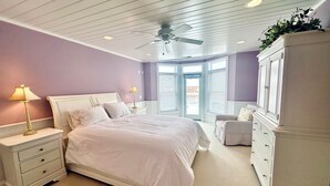 Une chambre à coucher avec un lit, des tables de chevet, une commode, un ventilateur de plafond et une vue par la fenêtre.