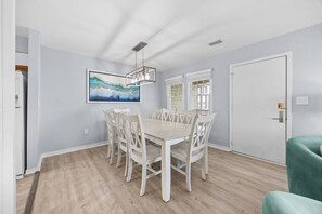 A dining room with a light-colored table and chairs, a modern pendant light, and a large abstract painting on the wall.