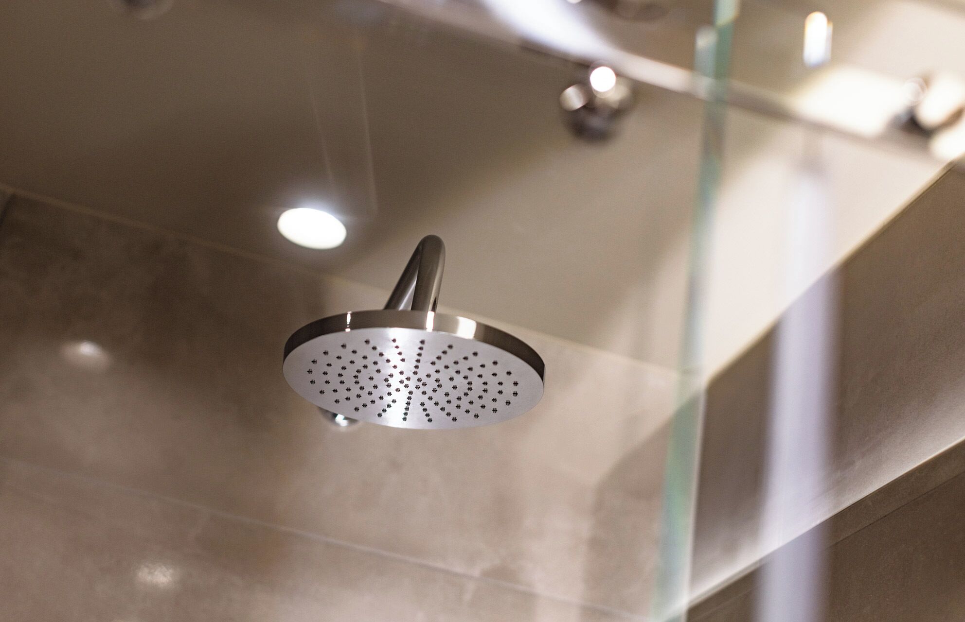 A showerhead with a modern design, mounted on a glass partition.