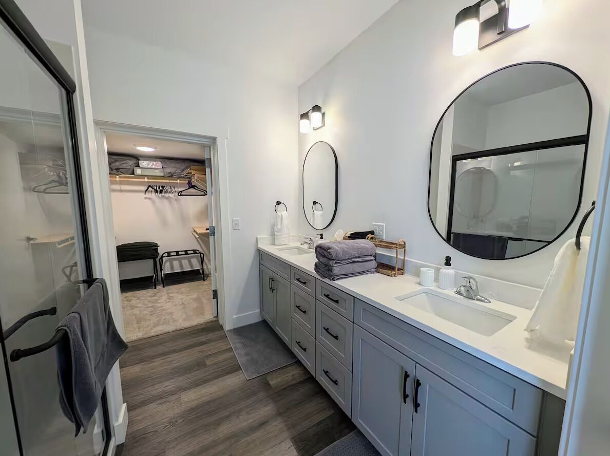 A modern bathroom with a large mirror, a sink, and a walk-in closet.