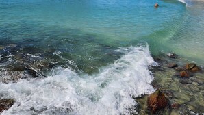 Ein Strand mit klarem Wasser, Wellen und Felsen.