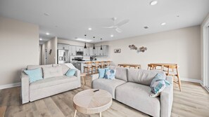 A modern living room with two grey sofas, a round coffee table, and a dining area with wooden chairs and a table. - Bayou Sunrise 3102 (Gulf Shores)