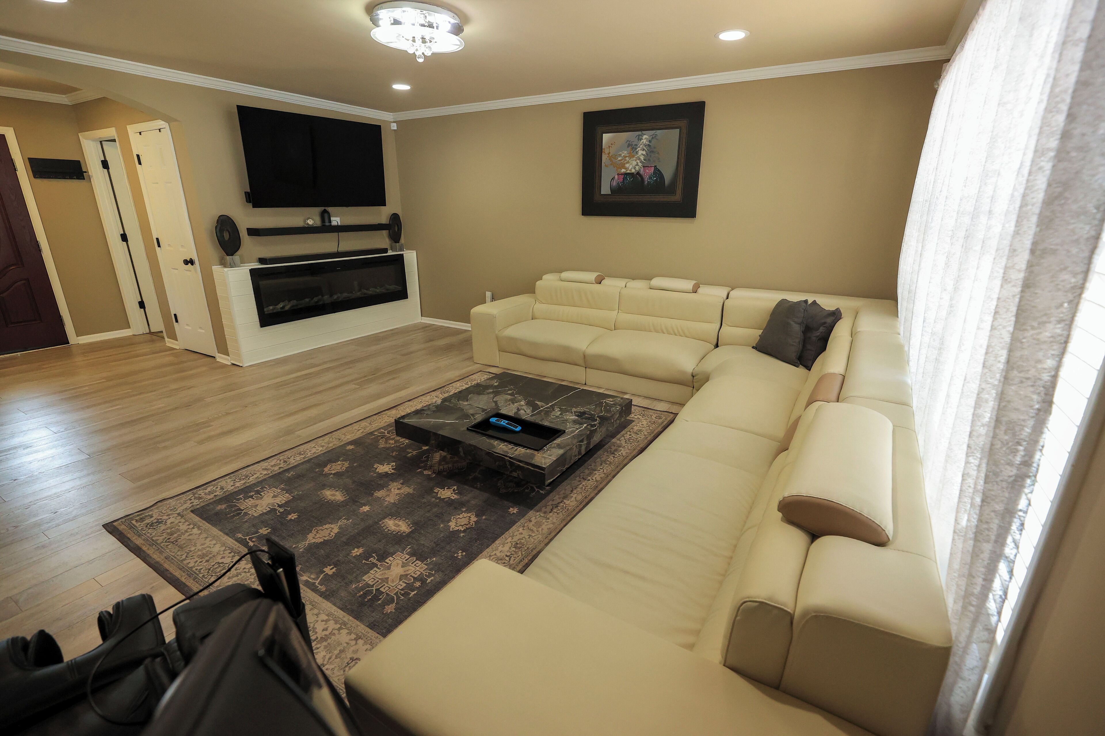 Un salon avec un canapé beige, un téléviseur à écran plat fixé au mur, une cheminée et un tapis à motifs.