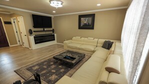 Un salon avec un canapé beige, un téléviseur à écran plat fixé au mur, une cheminée et un tapis à motifs.