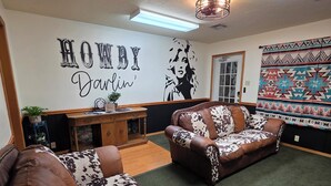 A living room with two brown leather sofas with cowhide patterns, a wooden coffee table, and a wall with a 'HOWDY Darlin'' sign.