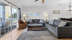 A living room with a sofa, armchair, coffee table, and a ceiling fan. There are two framed pictures on the wall and a chandelier. - Magnolia Place 4757-203 (Myrtle Beach)