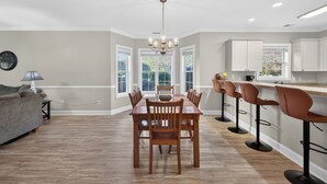 A modern kitchen with a dining area, featuring a wooden table and chairs, a chandelier, and white cabinetry. - Relax by the Pool Near Beach & Golf Courses | Magnolia Pointe Luster Leaf 4833-105 (Myrtle Beach)