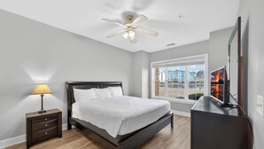 A bedroom with a bed, a nightstand, a lamp, a ceiling fan, a TV, and a window with a city view. - Relax by the Pool Near Beach & Golf Courses | Magnolia Pointe Luster Leaf 4833-105 (Myrtle Beach)