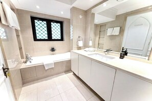 Un baño moderno con bañera, dos lavamanos, un espejo grande y una ventana con diseño de celosía.
