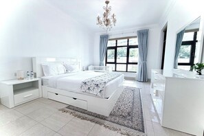 A modern bedroom with a large bed, bedside tables, a dresser, a chandelier, and a view through the window. - Burj Khalifa View Luxury 2BR Apartment Souk Al Bahar Downtown Dubai (Dubai)