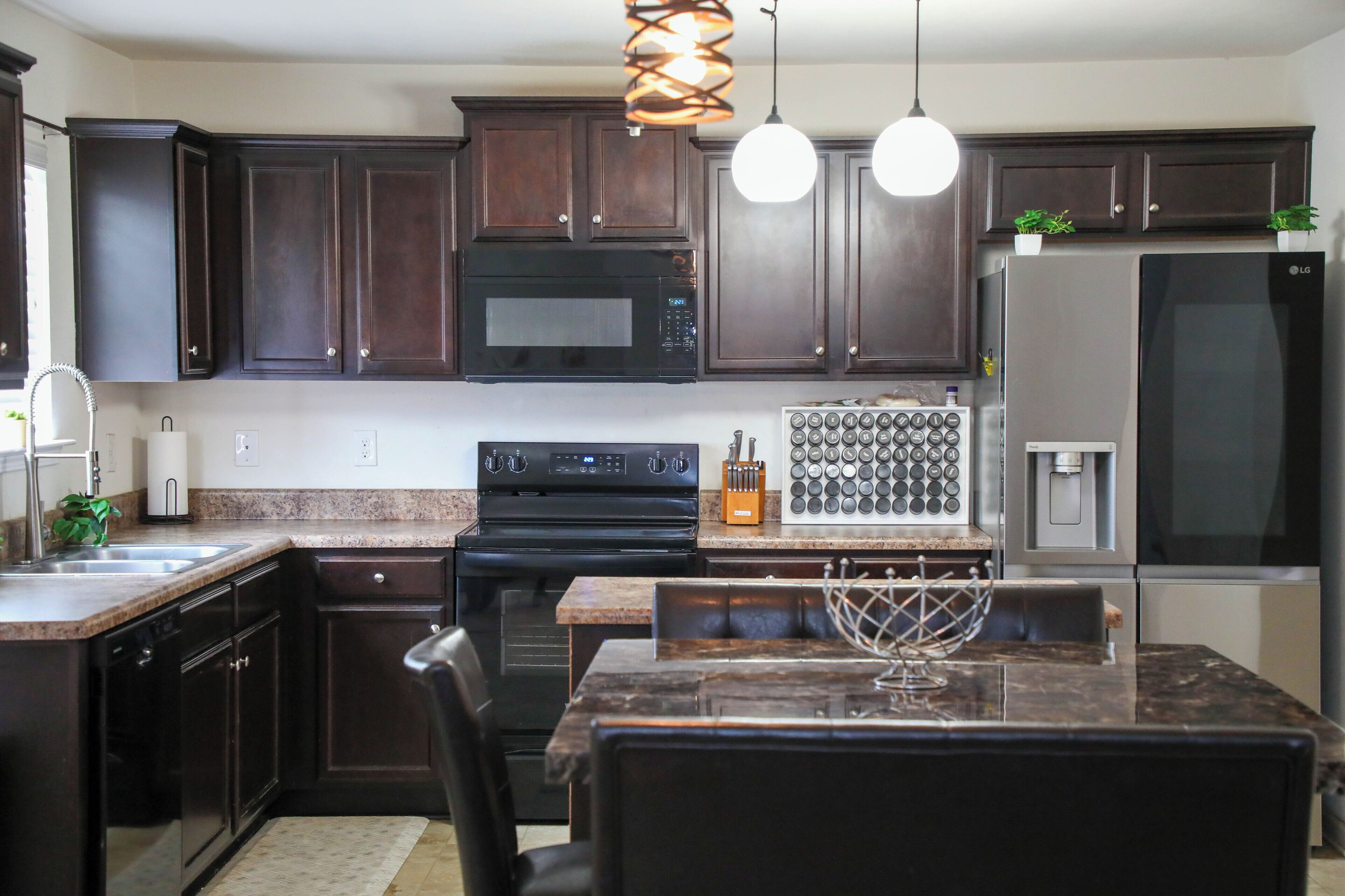 A modern kitchen with dark wood cabinets, a black microwave, a stainless steel refrigerator, and a central island with a wine rack.