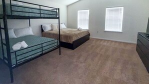 Une chambre avec des lits superposés, un ventilateur de plafond, deux fenêtres équipées de stores et une commode.