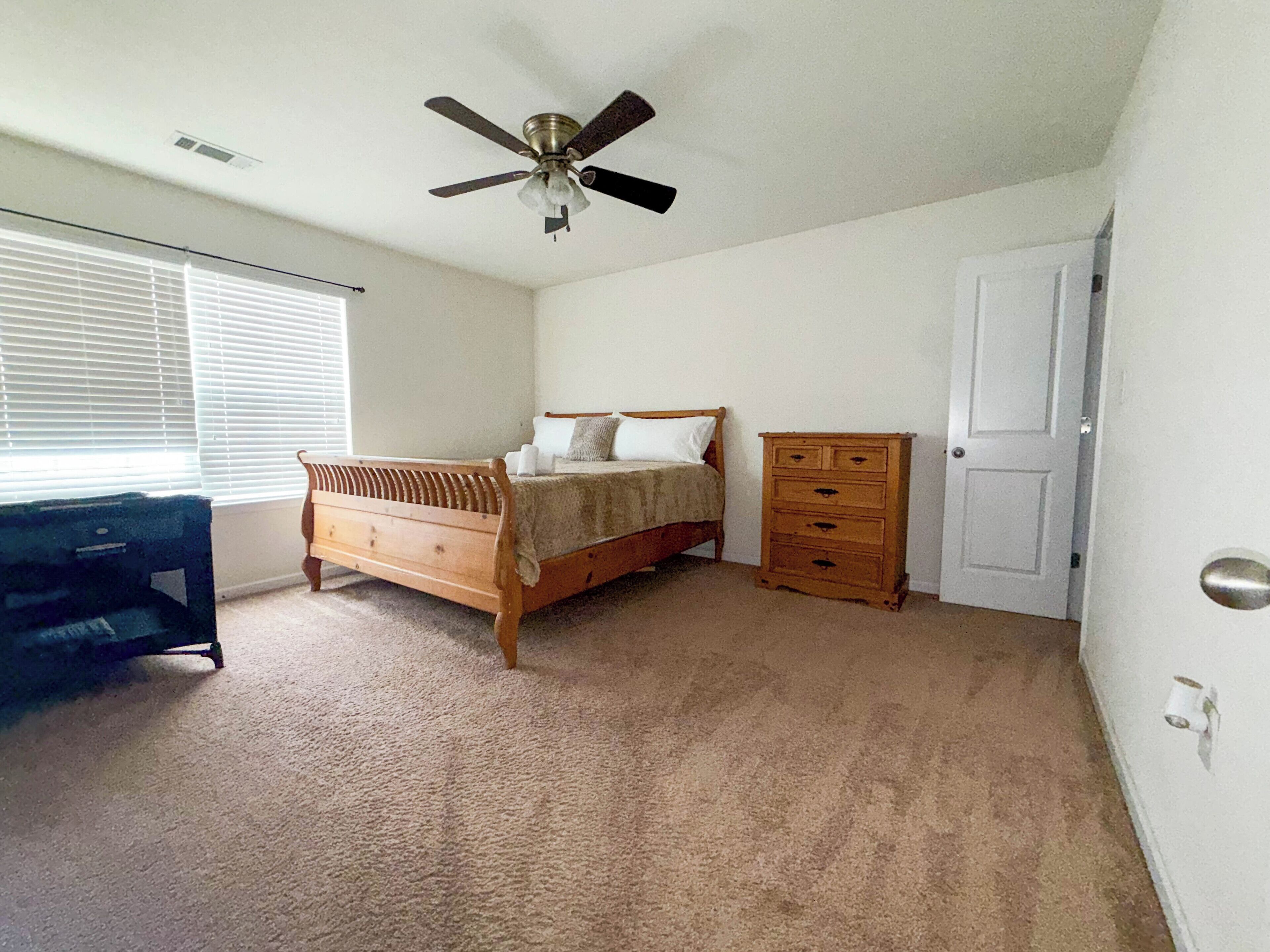 A bedroom with a bed, dresser, desk, and ceiling fan.