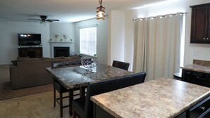 Une cuisine moderne dotée de plans de travail en granit, d’un coin repas avec une table et des chaises, d’un ventilateur de plafond et d’une cheminée.