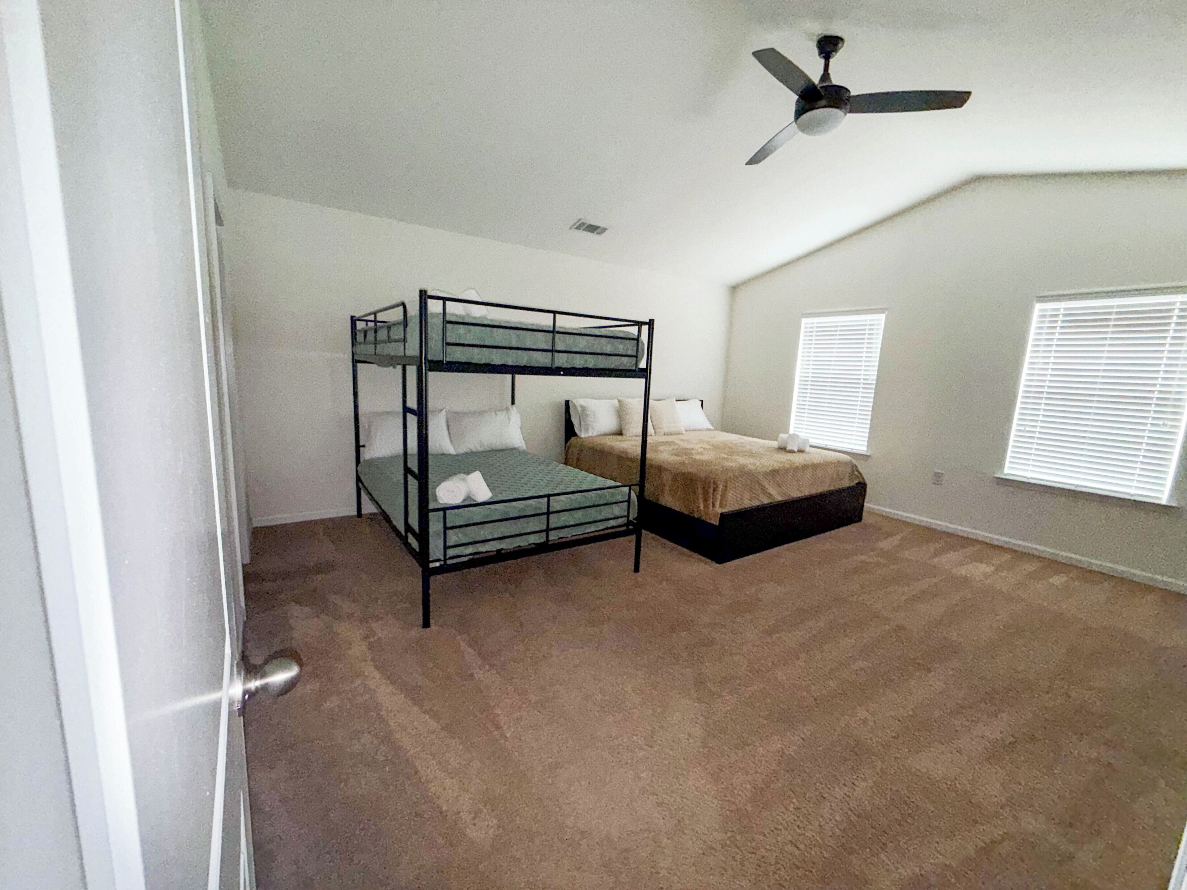 A room with a bunk bed, a ceiling fan, and a window with blinds.