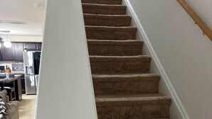 Un escalier recouvert de moquette, avec une rampe blanche, menant à un palier.