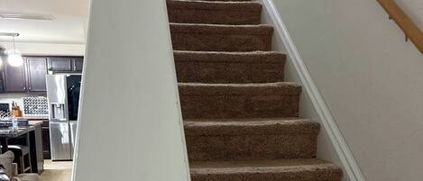 A carpeted staircase with a white handrail leading to a landing.