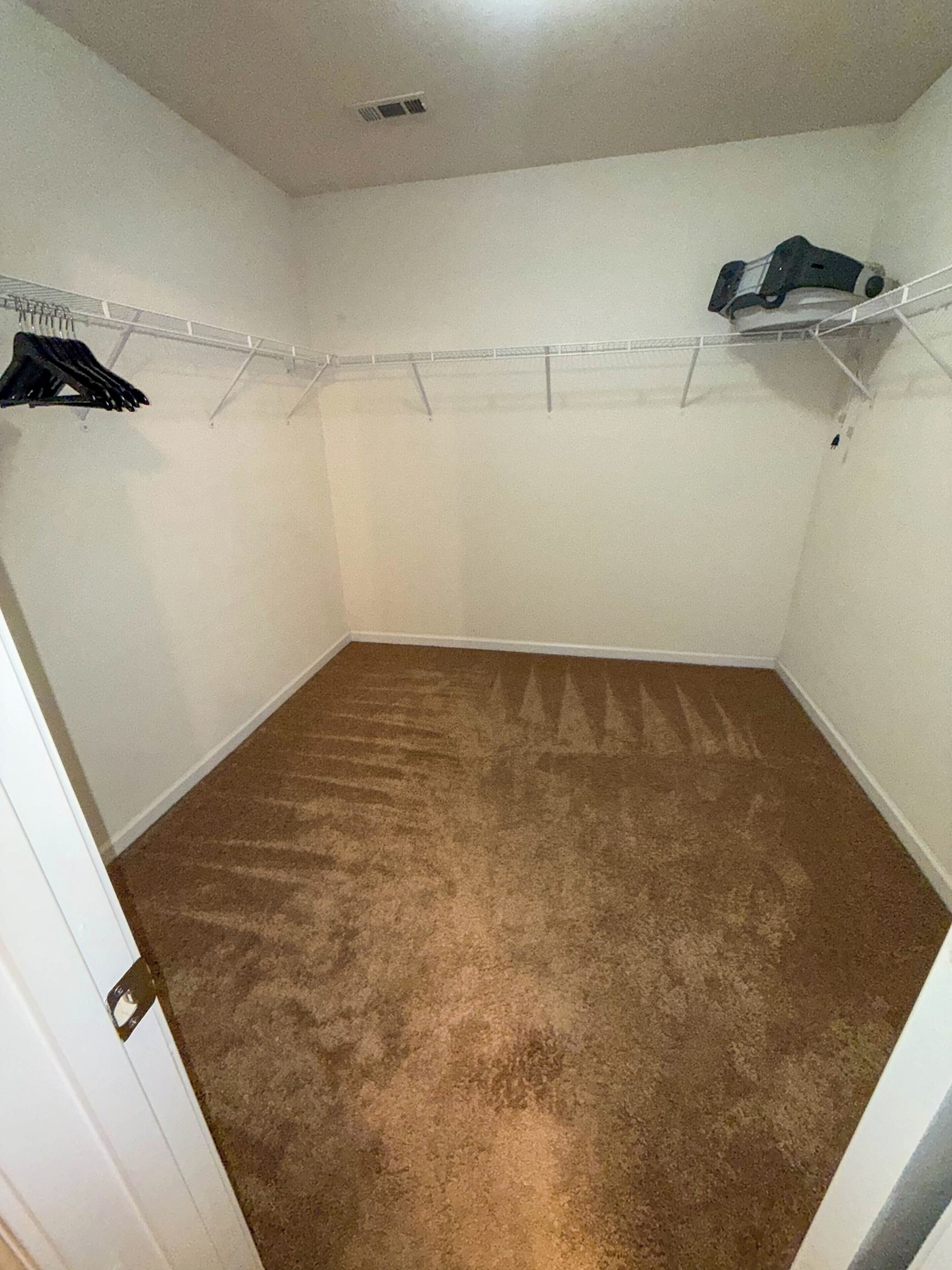 A room with a brown carpet, white walls, and a ceiling vent.