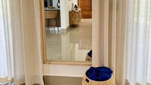 A room with a large mirror reflecting a dining area, a wicker basket, and a wooden door. - Brand-New 4BR with 5 beds Home in Bávaro Punta Cana-Private Pool (Punta Cana)