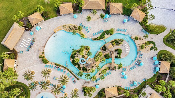 Vue aérienne d’un complexe hôtelier avec une piscine centrale, des chaises longues et des palmiers.