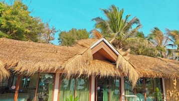 A thatched-roof structure with large windows, surrounded by palm trees.