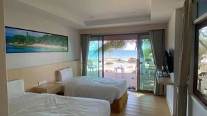 Une chambre d’hôtel avec deux lits, un tableau représentant une plage, une télévision et une vue sur la plage, visible à travers une porte vitrée.