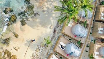 A beachside resort with palm trees, a sandy beach, and several large cylindrical structures, possibly water tanks.