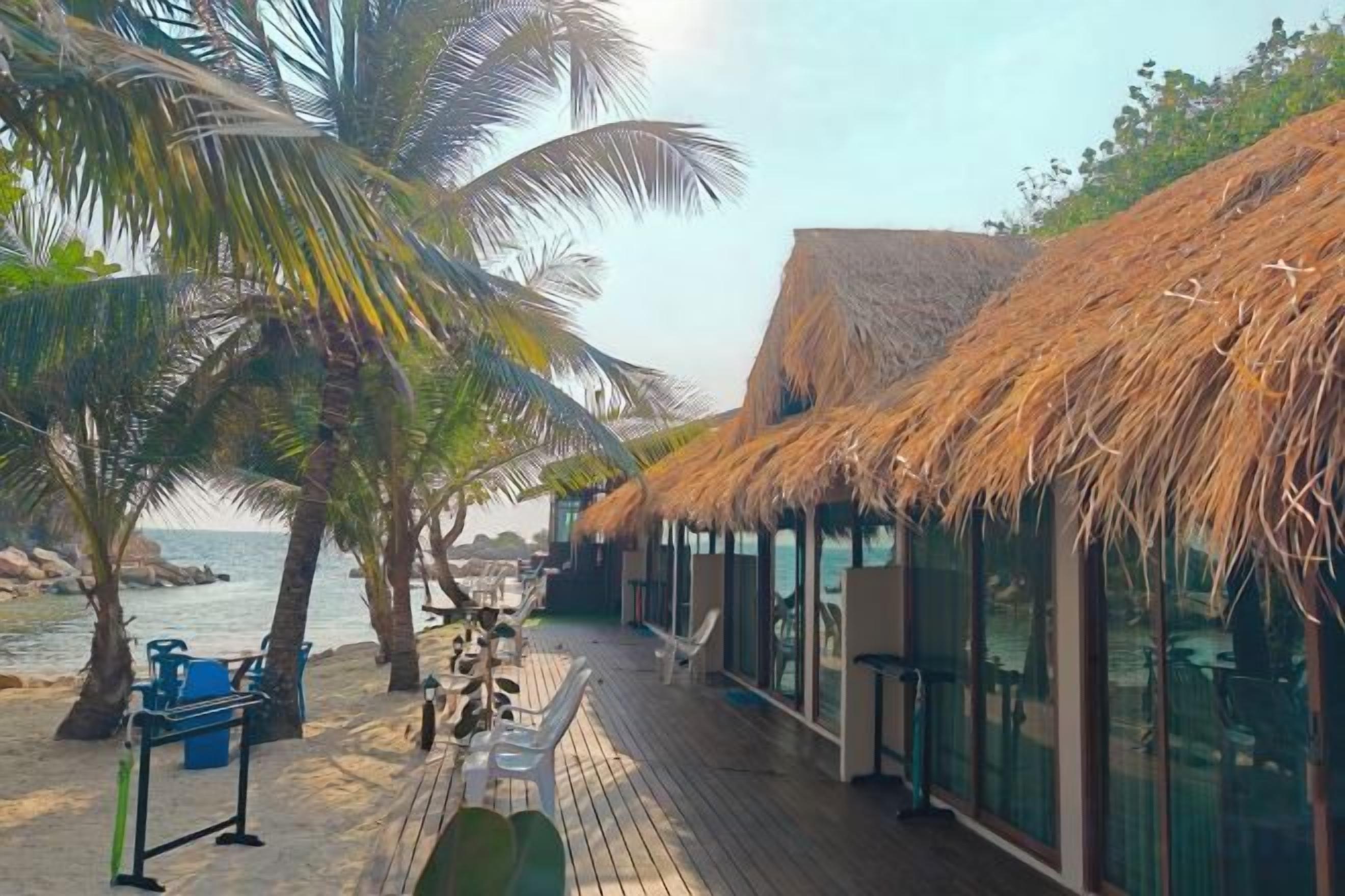 A beachside resort with thatched-roof structures, a wooden deck, and palm trees.