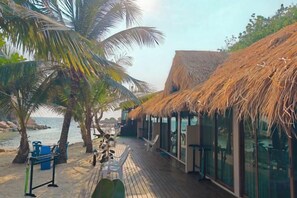 Un resort frente al mar con estructuras de techo de paja, una terraza de madera y palmeras.