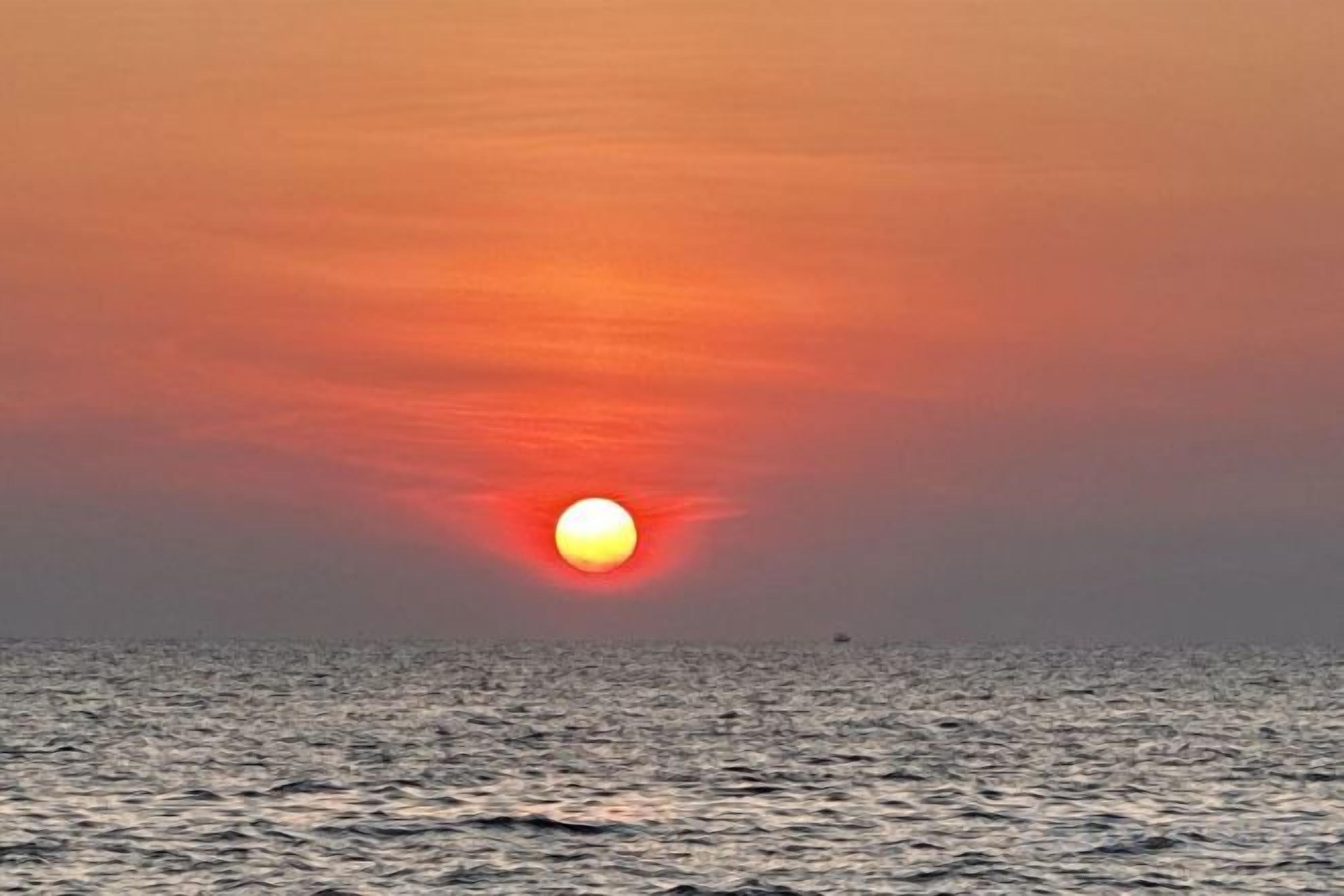 A sunset over the ocean with calm water and a clear sky.