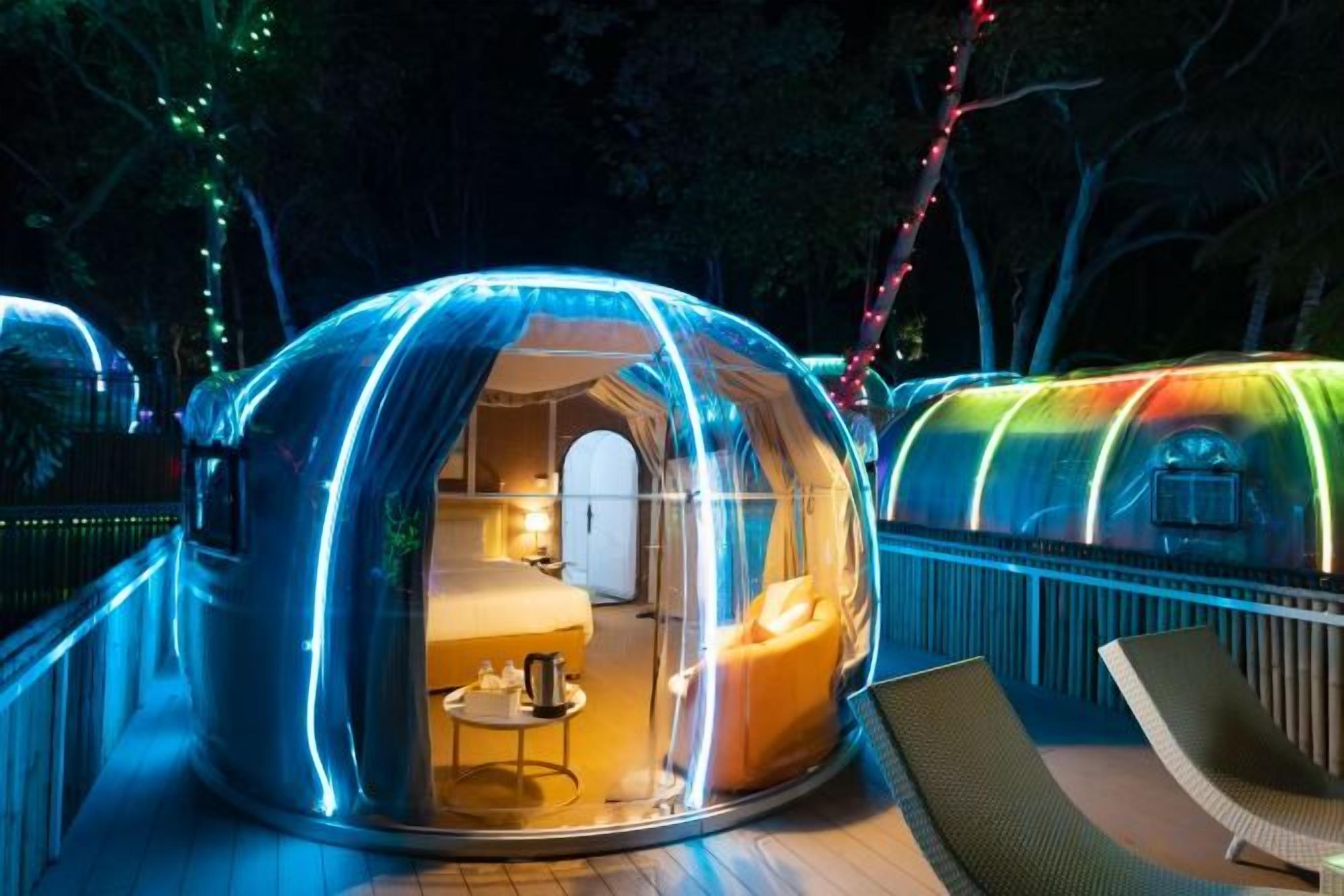 A transparent dome-shaped structure with a visible interior containing a bed, a table, and a chair.