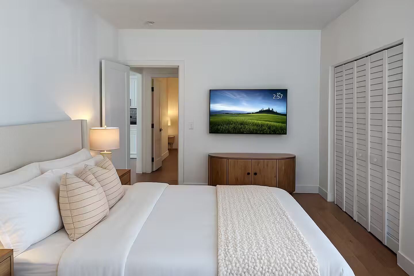 Een hotelkamer met een bed, een aan de muur bevestigde televisie, een kledingkast en een deur naar een gang.