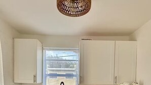 Une cuisine avec des meubles blancs, un plan de travail en bois, une fenêtre donnant sur un beau paysage et un luminaire suspendu.