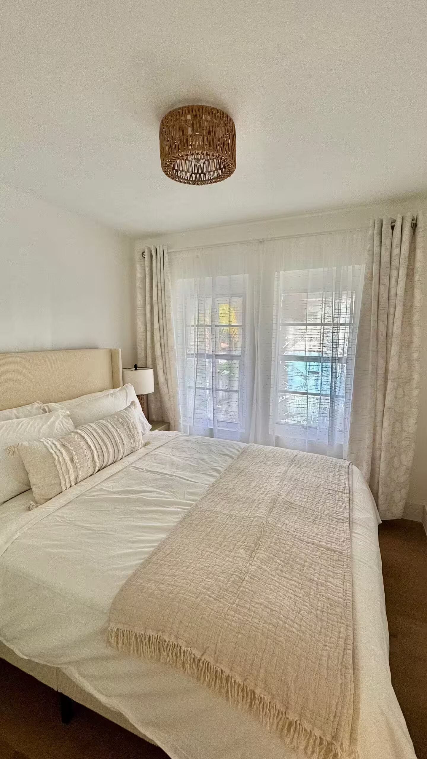 A bedroom with a large bed, a bedside lamp, and sheer curtains on the windows.