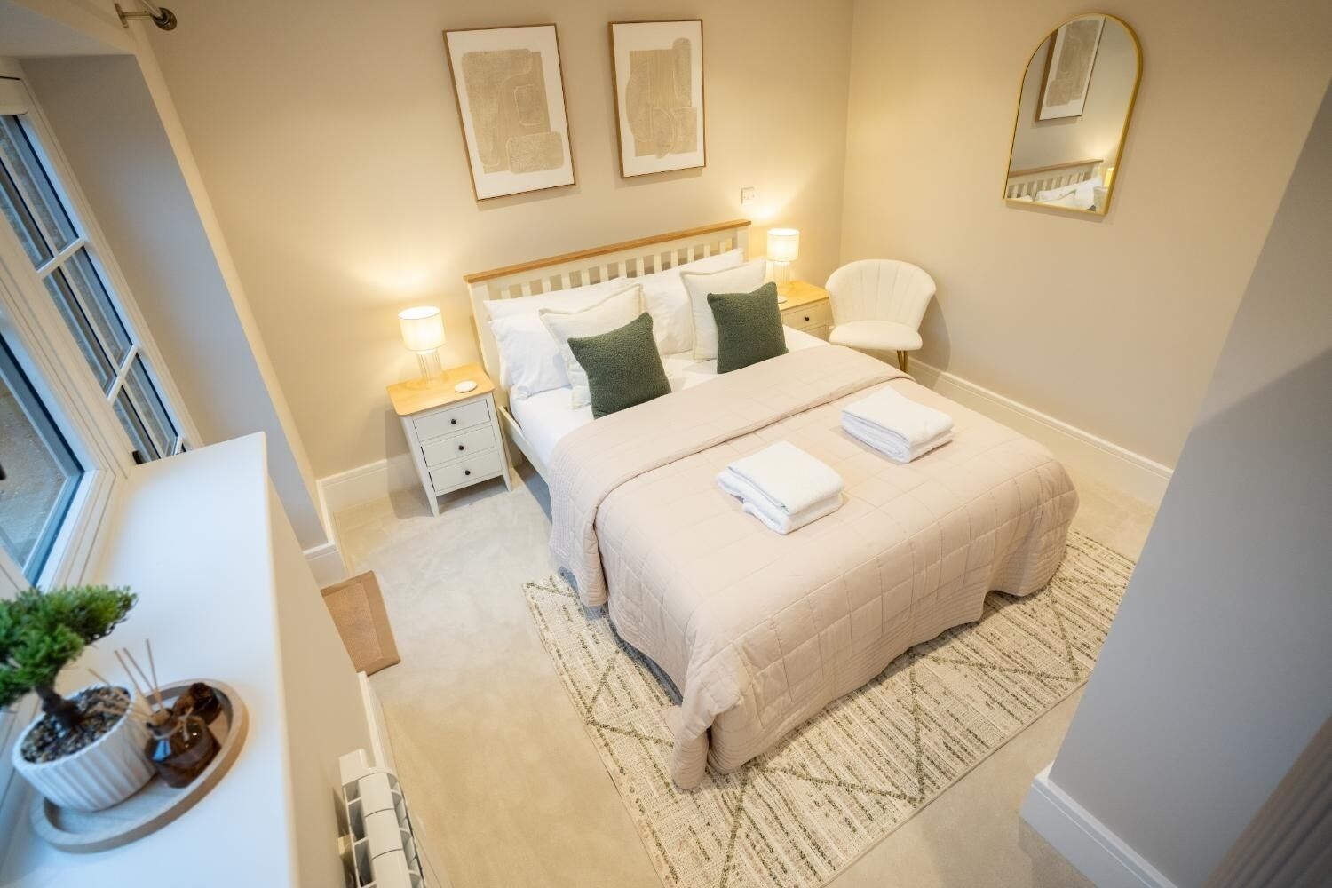 A bedroom with a bed, bedside tables, a chair, a mirror, and artwork on the wall.