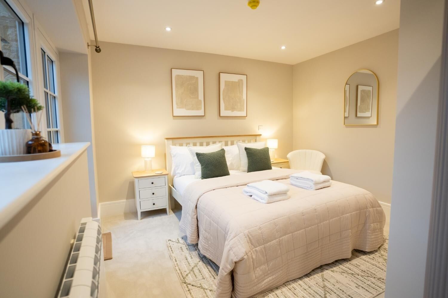 A bedroom with a bed, bedside tables, a nightstand, a window with a view, and wall-mounted artwork.