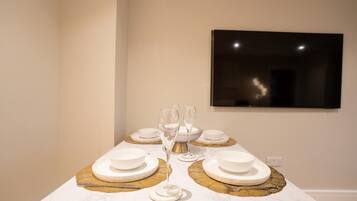 A dining table set with white plates, bowls, and glasses, with a gold placemat and a framed picture on the wall behind.