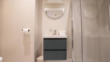 A modern bathroom with a toilet, a sink with a mirror above it, and a glass shower enclosure.