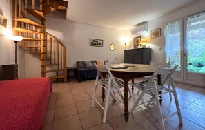 Ein gemütliches Zimmer mit einer Holztreppe, einem Esstisch mit Stühlen, einer Couch und einem Bett mit roter Decke.