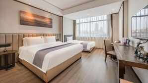 Una camera d'albergo con due letti, una scrivania e un'ampia finestra con tende.