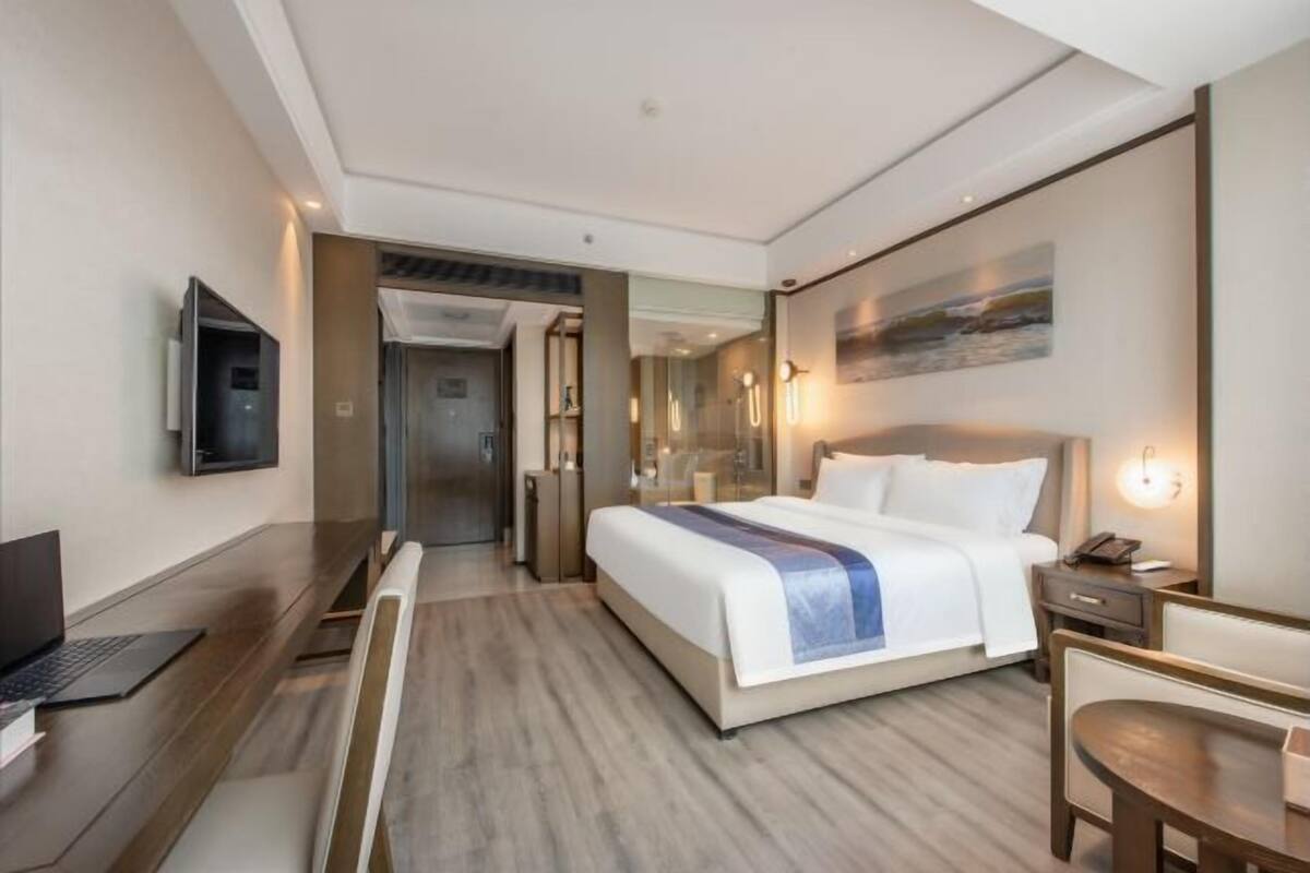 Ett modernt hotellrum med en stor säng, ett skrivbord, en platt-TV och en tavla på väggen.