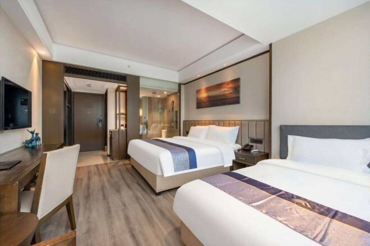 Ett hotellrum med två sängar, ett skrivbord, en stol, en tv och en tavla på väggen.