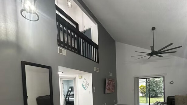 A spacious living area with a high ceiling, a staircase to an upper level, a large mirror, and a view through a glass door to the outdoors. - Beautiful and modern single home located 5 minutes from Indian Rocks Beach . (Largo)
