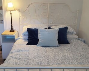 A bed with a patterned bedspread, two pillows, a bedside lamp, and a white nightstand. - Central to Vancouver Island. Easy Access to forest & river beaches, Pet friendly (Courtenay)