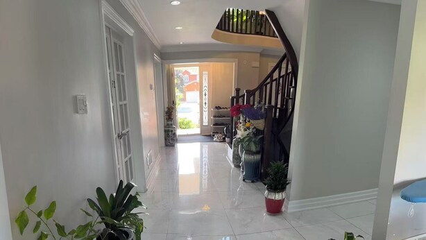 A spacious hallway with a polished tile floor, potted plants, and a staircase leading to an upper level. - Private Master Bedroom on second floor (Mississauga)