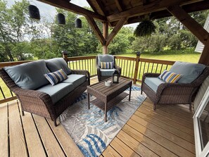A covered deck with wicker furniture, a coffee table, and hanging lanterns. - Charming 4-bedroom house with big yard in Poultney (Poultney)