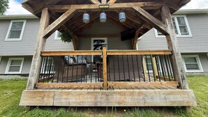A wooden porch with a railing, a bench, and a hanging plant. - Charming 4-bedroom house with a big yard in Poultney (Poultney)
