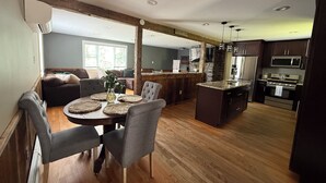 A modern kitchen with dark cabinetry, a central island, and a dining area with a round table and chairs. - Charming 4-bedroom house with a big yard in Poultney (Poultney)