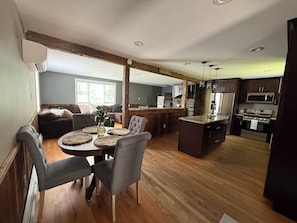 A modern kitchen with dark cabinetry, a central island, and a dining area with a round table and chairs.